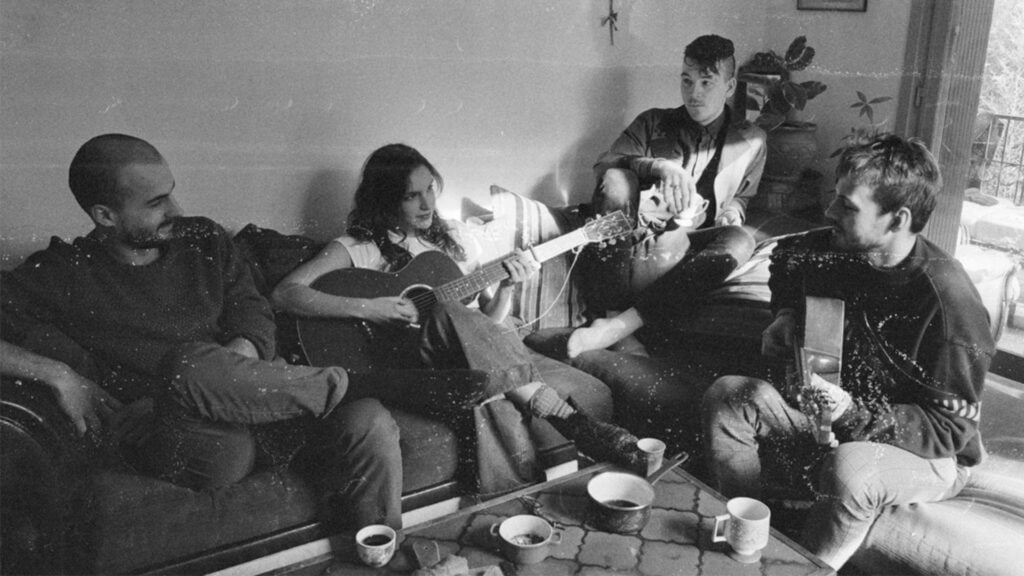 dans un appartementéclairé par un rayon de soleil provenant d'une fenêtre hors champ à droite, sur un sofa et dans un grain de photo noir et blanc très seventies, la chanteuse guitare folk entre les mains joue en souriant entouré de ses musiciens qui l'accompagnent, sourire et décontraction se lisent dans leur attitude